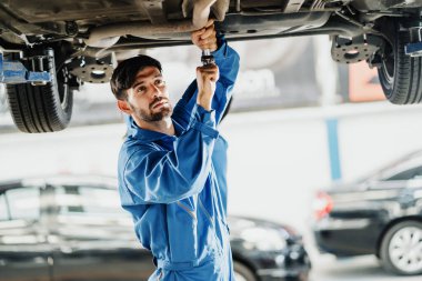 Üniformalı bir tamircinin portresi otomobil servisindeki bir arabayı tamir ediyor. Araba servisi, onarım, bakım ve insan konsepti.