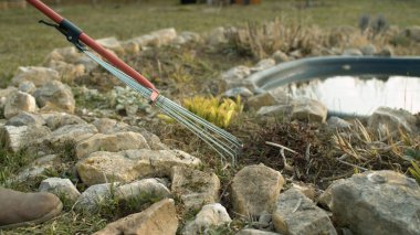 Çiçek tarlasında eski otları toplamak için tırmıkla. Bahçede bahar işi. Gölün yanındaki bahçede çalışan bir adam. Çevre dostu. Dünya günü.