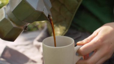 Bir kadın açık havada fincana kahve dolduruyor.