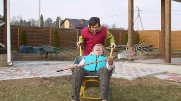 Homem empurrando sua mãe em um carrinho de mão — Vídeo de Stock