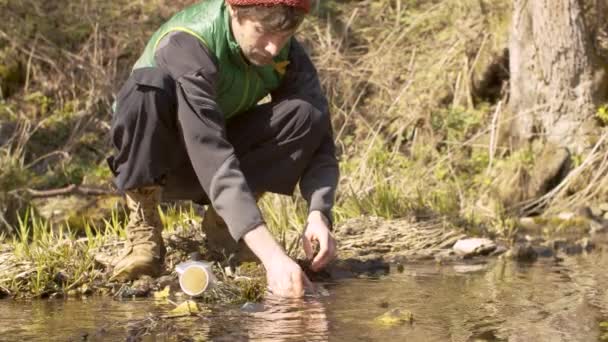 Young man washes the dishes in a forest river — Stock Video