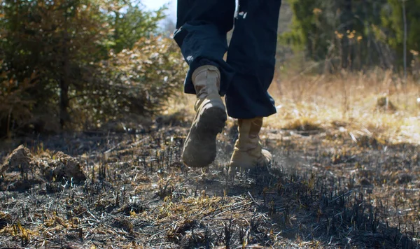 絶滅した森林火災の代わりに歩いてトレッキングブーツで男の足を閉じます 焼き草 灰の階段から上昇する — ストック写真