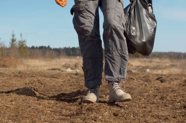 Elinde çöp torbası taşıyan bir çevre gönüllüsünün bacaklarını kapat. Genç çevreci gönüllüler plastik topluyor. İlkbaharın başlarında, orman açıklığında. Dünya günü. Çevre dostu kavram