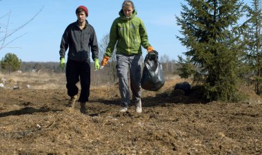 Ormanın yakınlarında yürüyen iki genç çevreci gönüllü. Elinde çöp torbası taşıyan bir kadın. Parlak mavi gökyüzü, ağaçlarda yaprak yok, yeşil köknar ağaçları. Dünya günü. Çevre dostu kavram