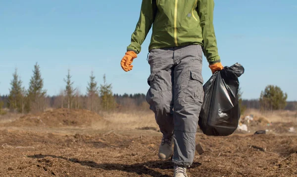 把一个提着垃圾袋的生态志愿者的腿绑起来 年轻的生态志愿者选择塑料 森林一片荒芜 地球日生态友好概念 — 图库照片