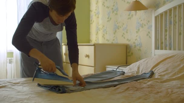 Unge man stryker jeans på sängen — Stockvideo