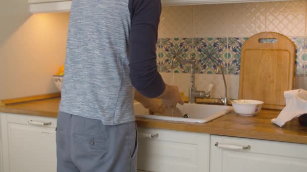 Молодой человек моет посуду на кухне — стоковое видео