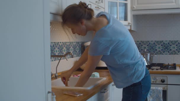 Νεαρή γυναίκα καθαρίζει ένα μπλοκάρισμα στο νεροχύτη της κουζίνας — Αρχείο Βίντεο