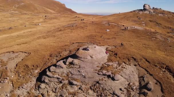Vue aérienne 4k de touristes assis sur un gros rocher sur le plateau montagneux de Bucegi avec le monument Sphinx en arrière-plan en Transylvanie, en Roumanie, en Europe, en orbite à gauche 