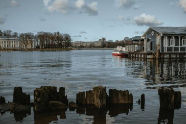 Nehir rıhtımındaki otantik kayıkhanenin estetik bir manzarası. Park etmiş kırmızı yatı olan yeşil renkli ahşap bir bina. Suda yansıma. Bulutlu gökyüzü. Seyahat ve yelken konsepti. Nehir manzarası