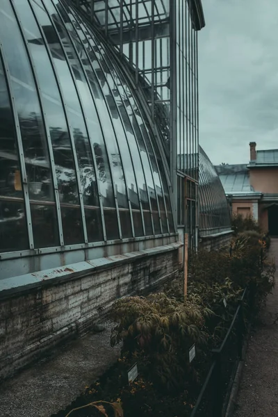 The Botanical garden building, glass facade greenhouse. Vintage architecture. The roof of glasshouse with the gloomy sky. Exterior with steel, angles, streamlined surface. A house for plants.