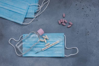 Tıbbi maske, tıbbi koruyucu maske, antiseptik, termometr, mavi arka planda haplar. Sağlık sigortası tıbbi tek kullanımlık yüz maskesi ağız ve burnu kapatıyor. Coronavirus karantinası, hijyen konsepti