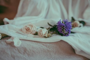 Beyaz yaprakların arasında keten bir çarşaf üzerinde beyaz güllerin yakın plan kompozisyonu. Çiçeksel konsept arka plan, kopyalama alanı. Yumuşak bir sabah dekoru. Bej renkli bir çiçek buketi, katlanmış tarafsız bir kumaş. Yumuşak odak