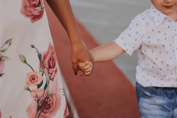Anne, sokakta yürürken küçük oğlunun elini tutuyor. Ebeveynlik ve aile yaşam tarzı kavramı.
