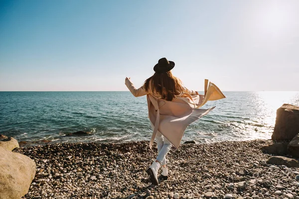 Bir kız plajda şapkası ve paltosuyla koşuyor.