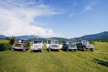 Bir yaz günü bir grup SUV aracını güzel dağların arka planına park etmek. Yolun dışındaki açık havada Jeep maceraları. Off-road araba gezisi..