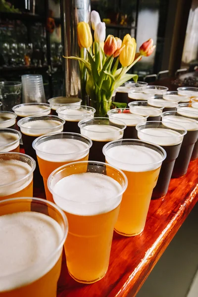 Tahta bir Pub Masasında Plastik Bira Bardakları. Bir sıra plastik bira bardağı ve bir partide bira..
