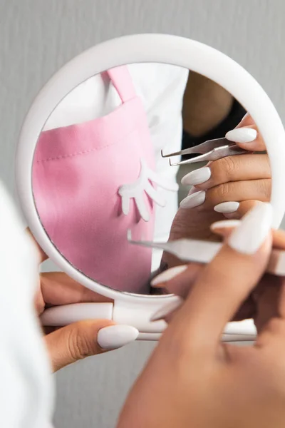 The girl's hands are masters of eyelash extension close-up. Reflection in the mirror of a hand with tweezers.