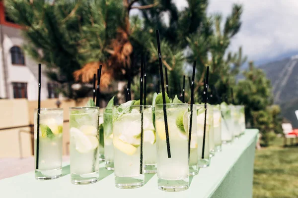 Yeşil yapraklı, şekerli ve limonlu mojito bardakları. Güneşli bir günde içkileri tazeliyorum. Bir yaz günü, dağların arka planında güzel kokteyller.
