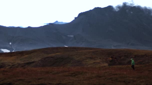Um homem caminha em um campo contra o pano de fundo de montanhas, nuvens e céu — Vídeo de Stock