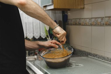 Genç bir erkek tencere içinde havuç pirzolasıyla kek hamurunu sallıyor. Kendi kendine fırında tatlı ya da kahvaltı.