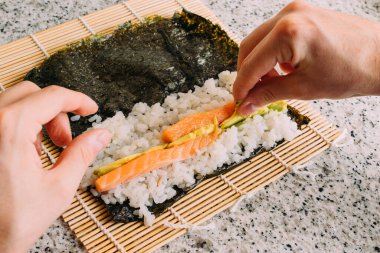 Somon balıklı maki suşi, avokado pilavı ve granit masada yosun yapıyorum. Japon yemeği pişirmek. Üst Görünüm.