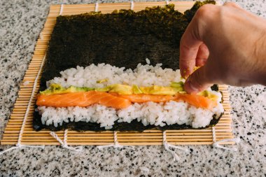 Somon balığı, avokado pilavı ve granit bir masada yosun ile maki suşi yaparken ön manzara. Japon yemeği pişiriyorum..