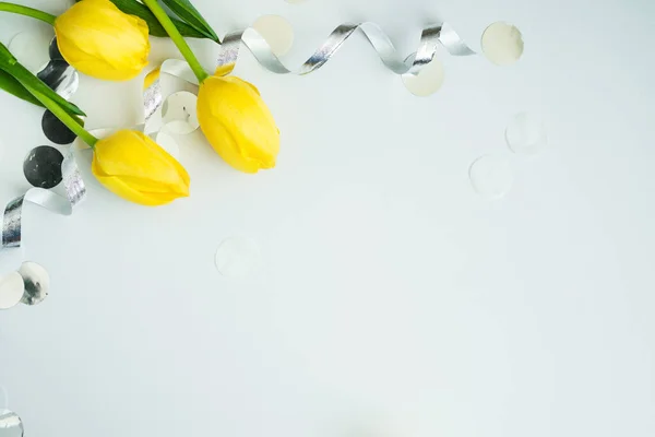 Painted Eggs, yellow tulips. silver serpentine and confetti with space for text on grey background, flat lay, Happy Easter, woman or mother day concept