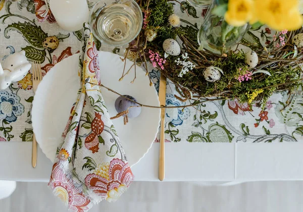 Feestelijke Tafel Met Bloementafelkleed Takkenkrans Kleurrijke Paaseieren Gele Tulpen Vaas — Stockfoto