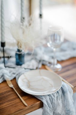 Tatil yemeği için minimalist masa, kurumuş çiçekli ahşap masa, tabaklar, altın çatal bıçak takımı, beyaz kanepeler, parlak mavi masa koşucusu. Seçici odak.