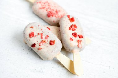 Çikolata kaplı çubuk üzerinde Eskimo dondurması ve beyaz taştan arka planda süblimleşmiş çilek. Lezzetli tatlı atıştırmalıklar. Yakın plan.