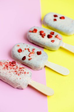 Çikolata kaplı çubuk üzerinde Eskimo dondurması ve sarı ve pembe arka planda kırmızı serpinti. Lezzetli tatlı atıştırmalıklar. Üst görünüm, yakın çekim, köşegen