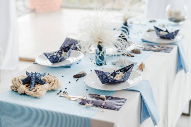 Festival masası için dekorasyon. Deniz tarzı. Zarif tabaklar, kağıt bardaklar, mavi tekstil. Şekerli kâğıt tekneler. Doğum günü veya bebek partisi çocuğu konsepti.