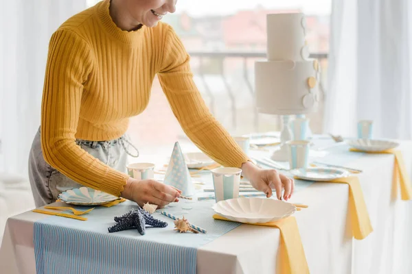 Parti masasında mavi, beyaz ve sarı renkli pastalarla servis yapan kadın, bantlı masa örtüsü, kağıt tabak, bardak ve altın çatal bıçak takımı. Erkek için doğum günü. Deniz konsepti