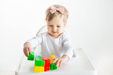 Anaokulunda renkli ve mantıklı oyuncaklar oynayan sevimli bir kız bebek. Bebek beyaz arka planda izole bir şekilde masada oturuyor..