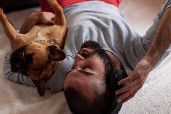 French Bulldog with young man with headphones smiling while lying on the floor at home