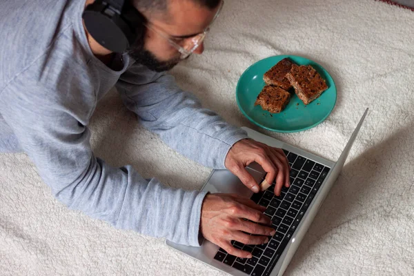Handsome young man listening music and using computer while resting on the floor and having breakfast. White background