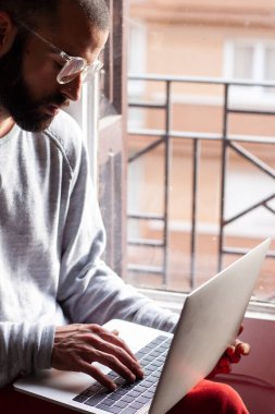 Gözlüklü genç adam, sabah erkenden bütün işlerini halletmek için dizüstü bilgisayarı üzerinde çalışıyor.