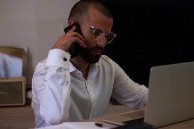 Mimar ev ofisinin bilgisayarında çalışırken bir telefon görüşmesi yapıyor.