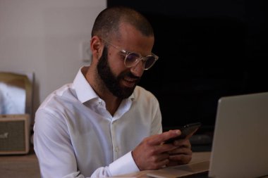 Ev ofisinde çalışırken bilgisayarındaki bilgileri kontrol ederken sakallı başarılı bir adam tatmin olmuş bir şekilde gülümsüyor.