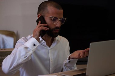 Mimar ev ofisinin bilgisayarında çalışırken bir telefon görüşmesi yapıyor.