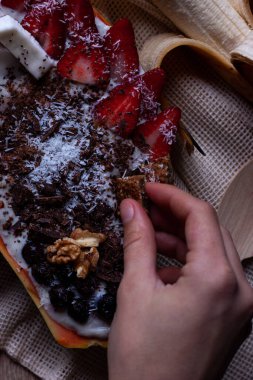 Papaya kasesinde sağlıklı kahvaltı yapan bir kadın. Mısır gevreğiyle yoğurt, taze çilek, yabanmersini, hindistan cevizi, çikolata, yoğurt ve chia çekirdeği..