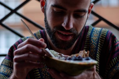 Papaya kasesinde sağlıklı kahvaltı yapan genç bir adam. Mısır gevreğiyle yoğurt, taze çilek, yabanmersini, hindistan cevizi, çikolata, yoğurt ve chia çekirdeği.