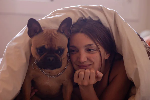 Happy woman with french bulldog while laying inside a bed