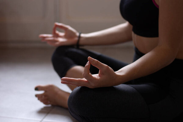 Close-up view of anonymous young woman doing morning yoga after waking up at home. Female model sitting cross-legged in Easy pose, Sukhasana posture and meditating.