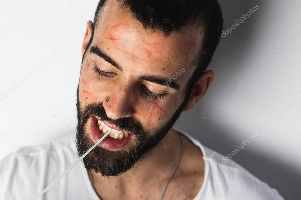 Handsome young man with traces of lipstick on his face playing with a gum