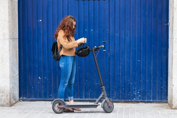 Mavi duvarın önündeki kadın elektrikli scooter 'a binmeye hazırlanıyor.