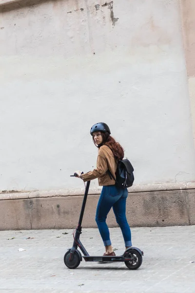 Kasklı ve sırt çantalı güzel bir kadın sokakta scooter kullanıyor.