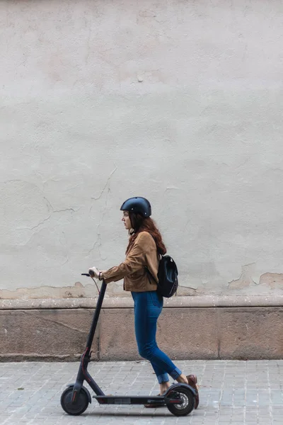 Pastel bir duvarın önünde elektrikli scooter süren güzel bir kadın.