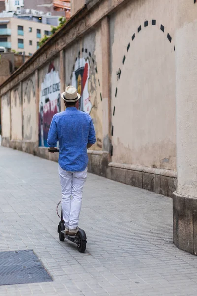 Şapkalı genç adam elektrikli scooterıyla şehri geziyor.